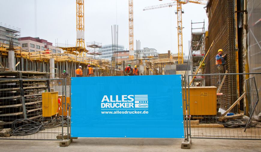 Bauzaunhusse vor einer baustelle Blaue Bauzaun Husse mit dem Allesdrucker Logo vor einer Baustelle